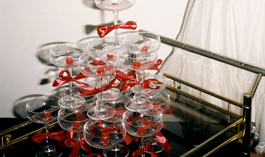 champagne tower of coupe glasses with red bows around the stems, all placed on a cocktail trolley