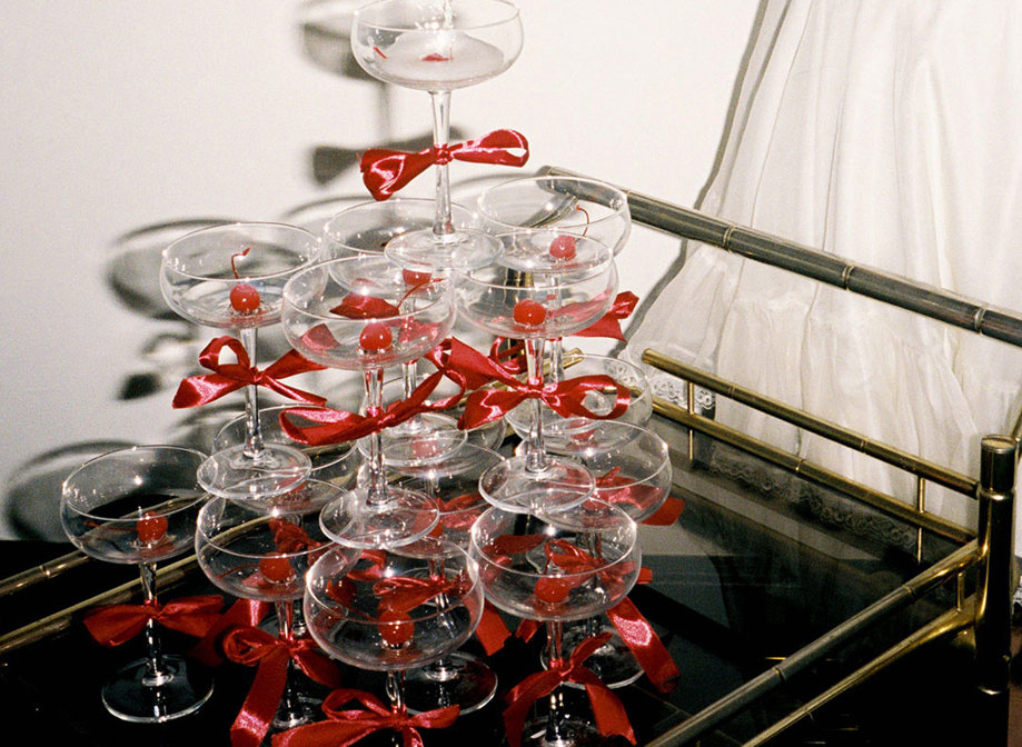 champagne tower of coupe glasses with red bows around the stems, all placed on a cocktail trolley