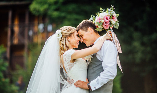 A bride and groom stand with their arms around each other and the bride is holding a white and pink bouquet