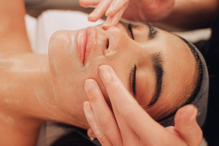 close-up of a woman's face as someone else's hands apply a product all over her face and neck