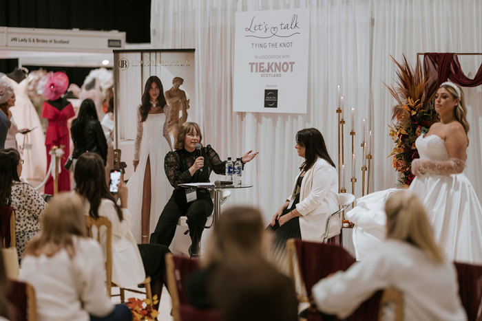 A person speaking to a person sitting at a table at The Scottish Wedding Show.