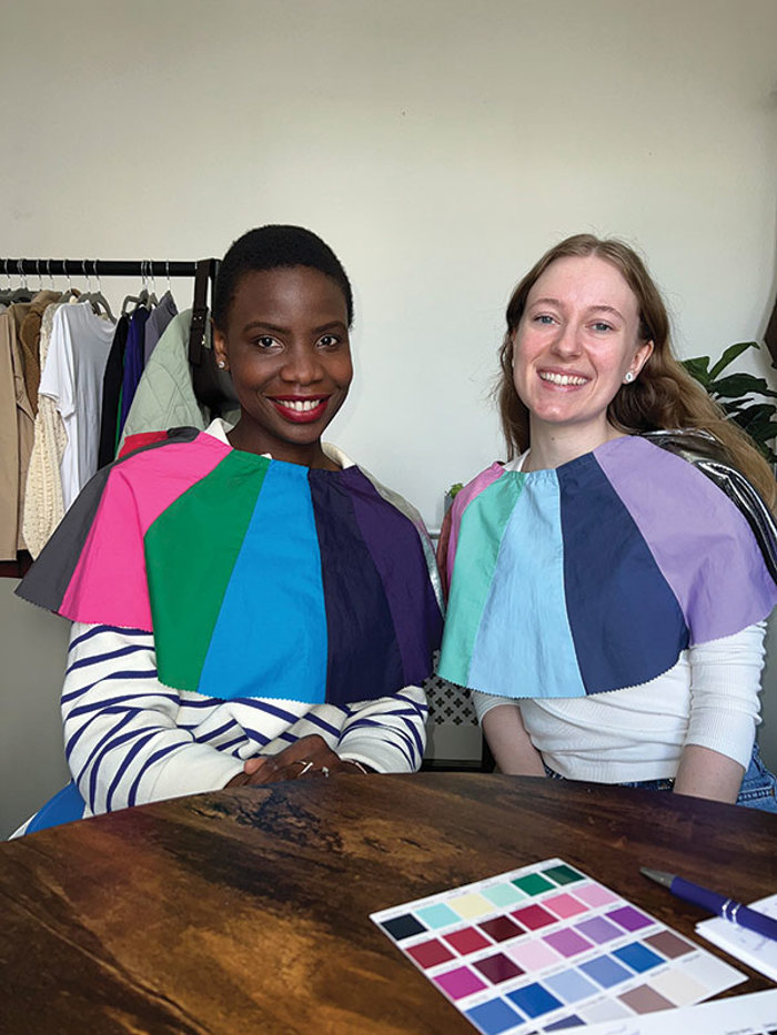 two women sit side by side with differently coloured fabric draped across their shoulders for comparison 