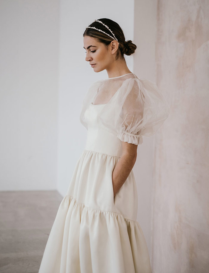 brunette woman wears a white strapless tiered floor-length gown with an organza puff sleeved top placed on top