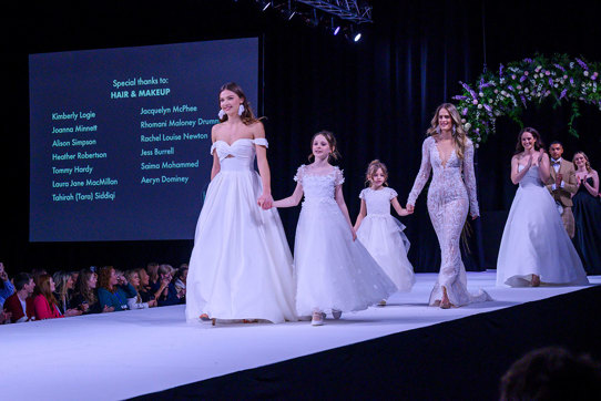 a catwalk with female models wearing wedding dresses and young girl models in frilly dresses too