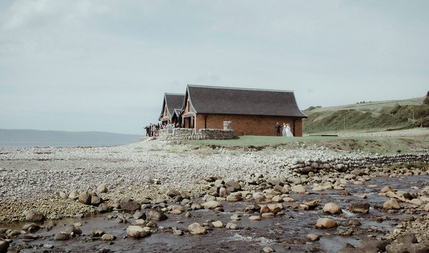 A group of people gathered outside Dougarie Boathouse with pebble beach in foreground