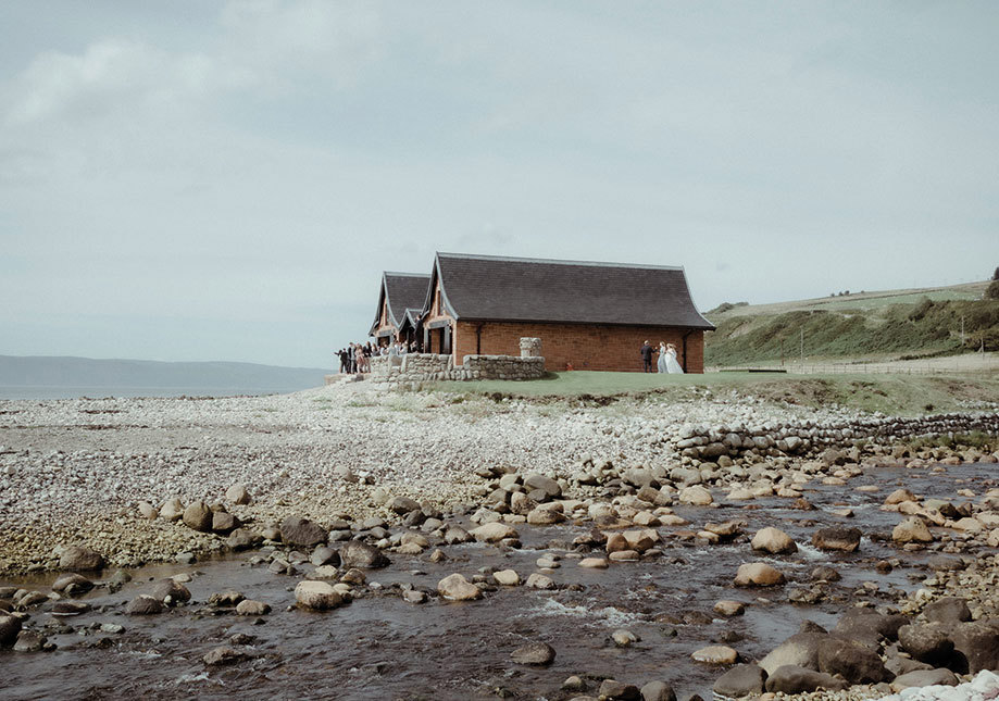 A group of people gathered outside Dougarie Boathouse with pebble beach in foreground