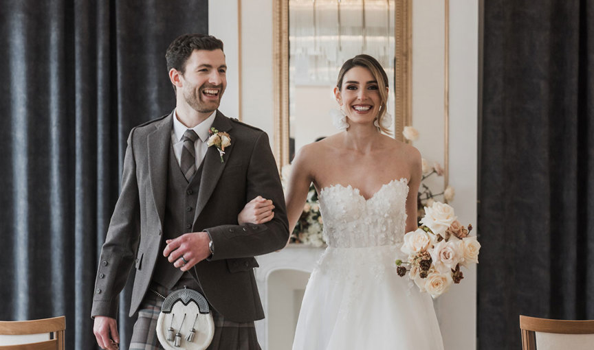 a bride and groom smiling and walking arm in arm up the aisle in the Gallery room at The Exchange Glasgow wedding venue