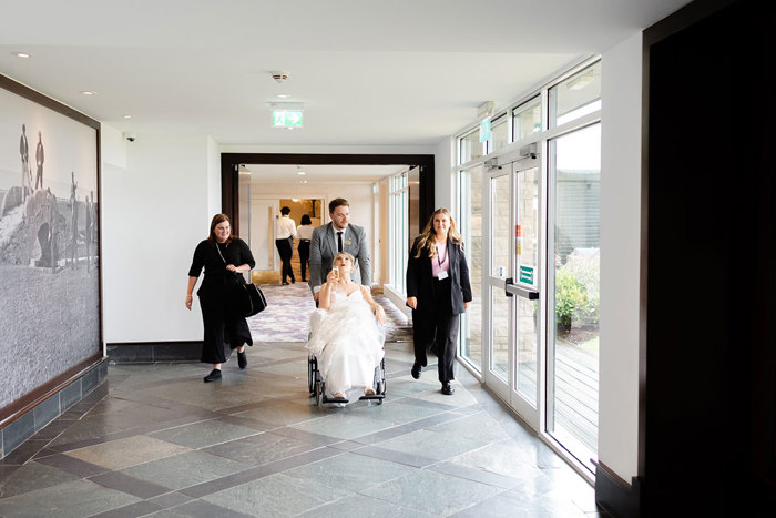 a bride being pushed along a corridor in a wheelchair