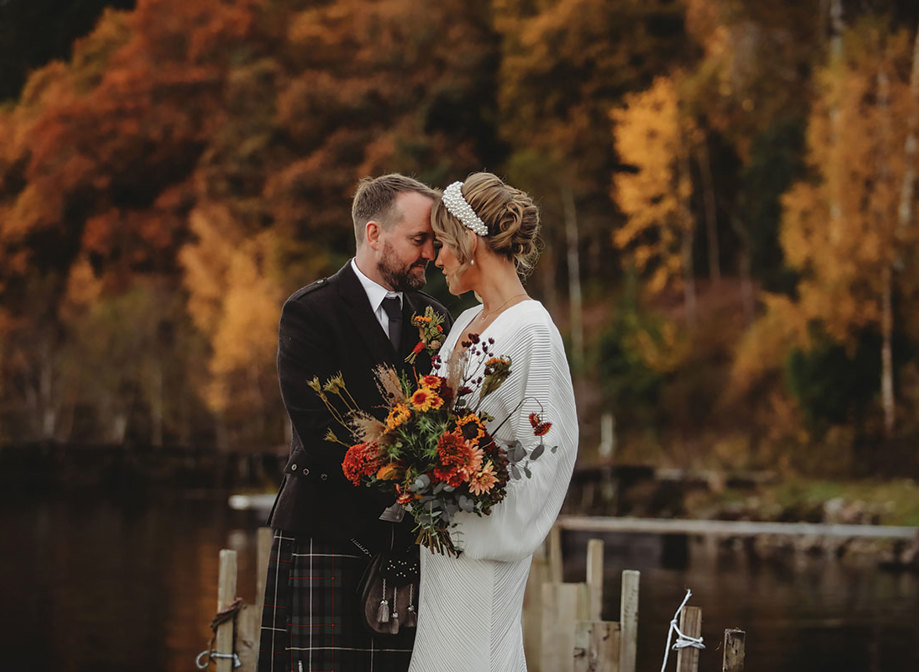 a bride and groom standing head to head with autumn trees turning gold and russet in background