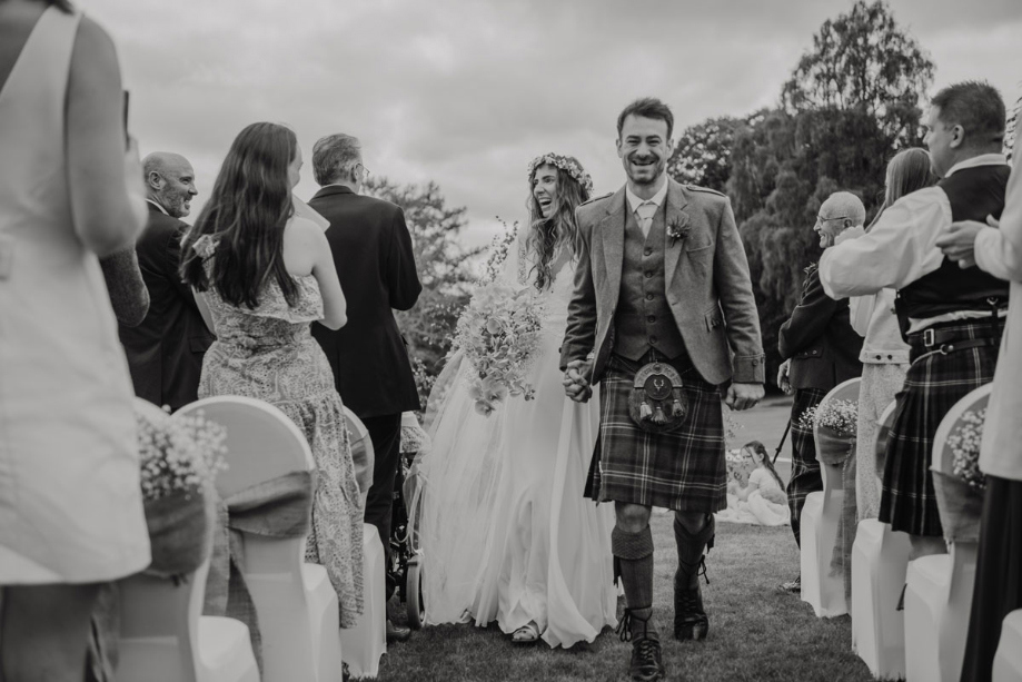 A Black And White Image Of A Bride And Groom Walking Up Aisle Outdoors At Raemoir House