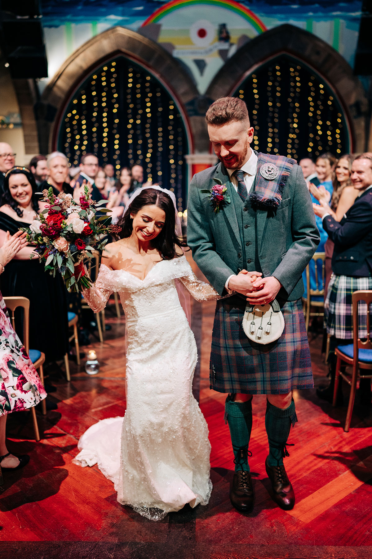 bride and groom dance up aisle during wedding day at oran mor as guests smile behind them