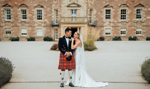 A bride in a wedding dress and a groom in a kilt standing in front of Archerfield House.