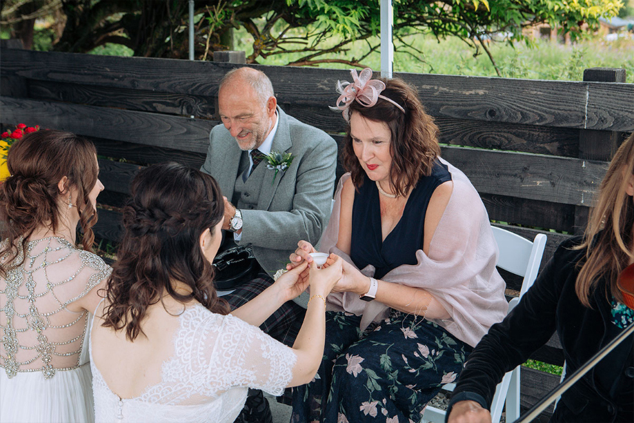 Two Brides Kneeling And Passing Tea Cups To A Man And A Woman