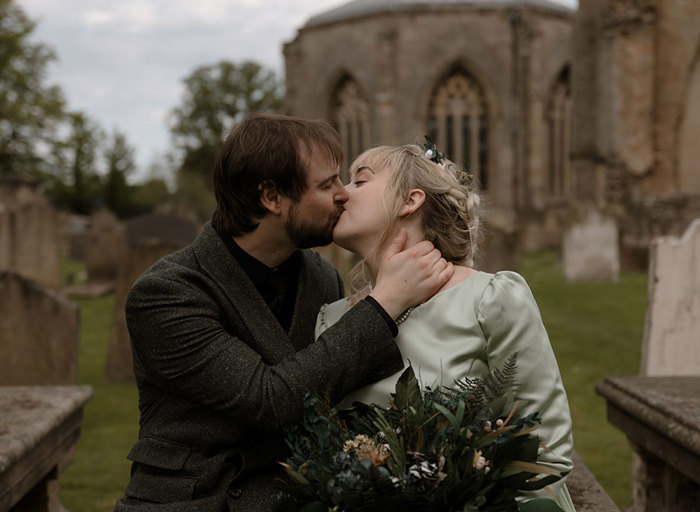 a bride and groom kissing in the grounds of Elgin Cathedral with gravestones in background