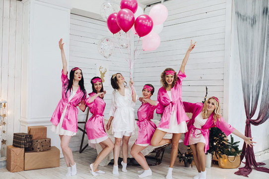 Group of women wearing pink robes pose on either side of woman in white robe 