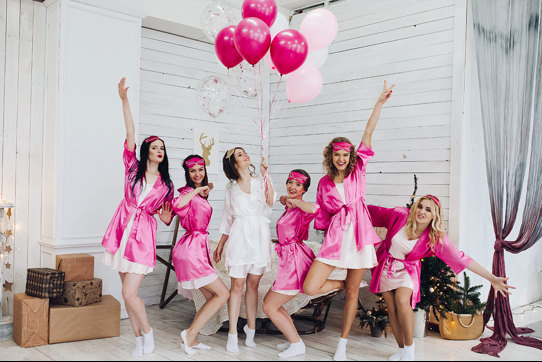 Group of women wearing pink robes pose on either side of woman in white robe 