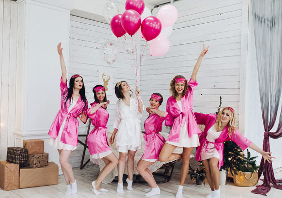 Group of women wearing pink robes pose on either side of woman in white robe 