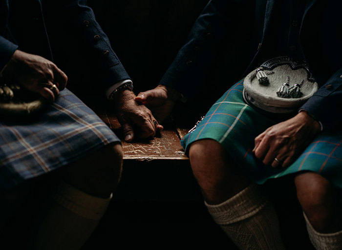 detail shot of two grooms wearing kilts holding hands