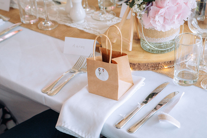 A Wedding Table Set For Dinner With Brown Paper Gift Bags At Place Setting