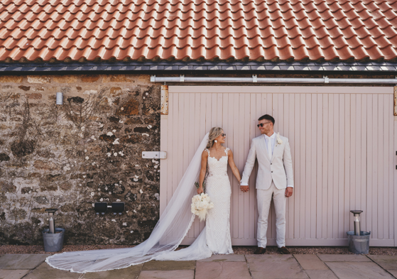 Bride and groom standing outside holding hands and wearing sunglasses