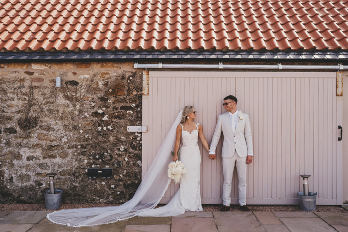 Bride and groom standing outside holding hands and wearing sunglasses