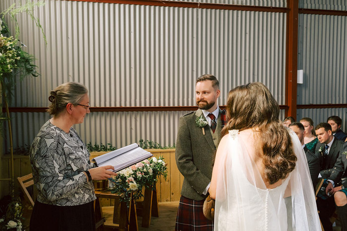 A celebrant reading during a cermony with the groom facing the camera and the bride facing the groom