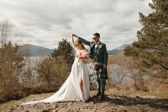 A Bride And Groom Dancing on a stony surface with trees, a lake and countryside in the background