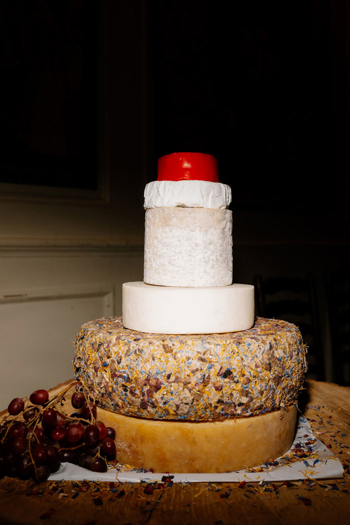 a tall stack of a variety of round cheeses with grapes in a dark room