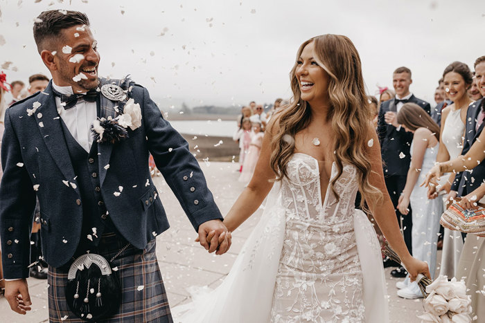 couple happy and smiling as guests throw confetti on them after wedding ceremony 