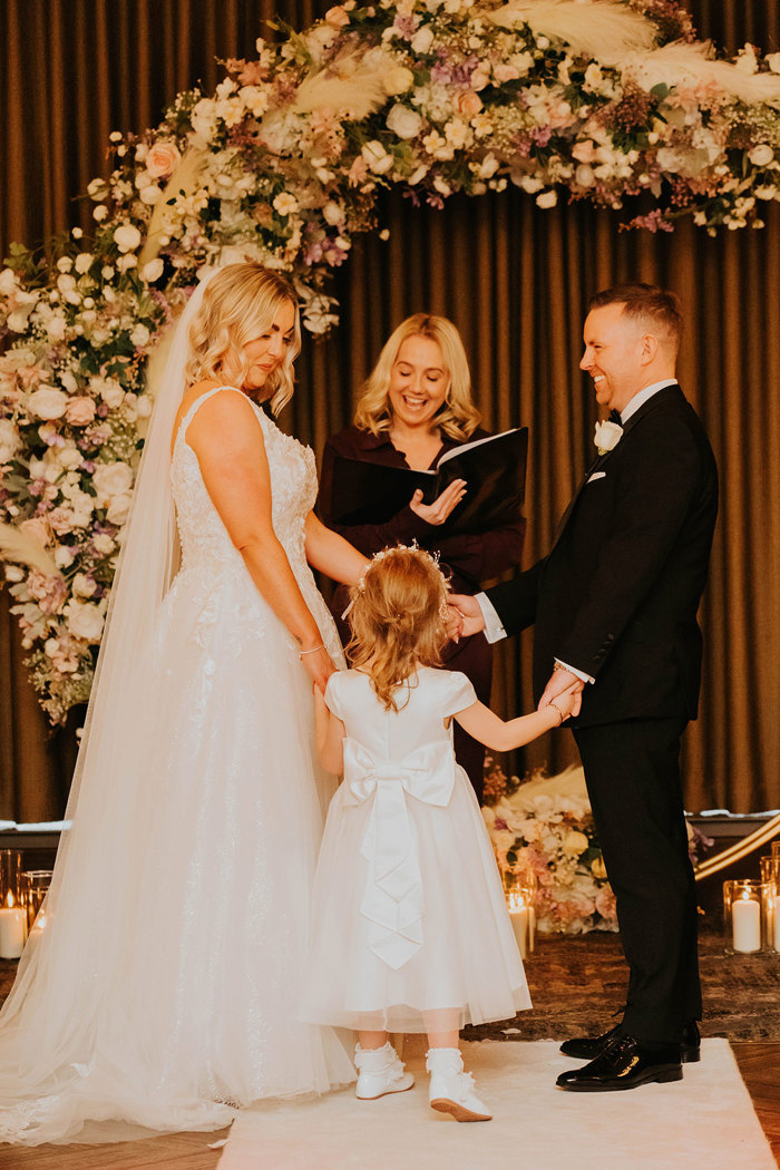 A bride and groom holding hands during a wedding ceremony and looking a child.