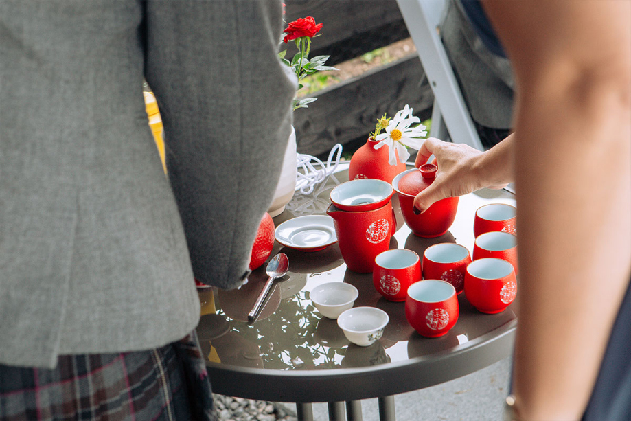 Hands Reaching For Red Chinese Tea Cups On A Tray On A Table