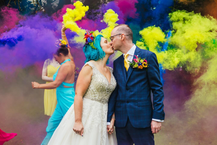 a couple kiss as people set off colourful smoke canons behind them