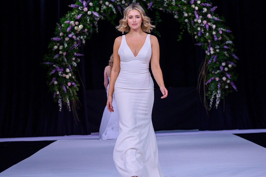 a model wearing a plain unadorned wedding dress walking down a catwalk