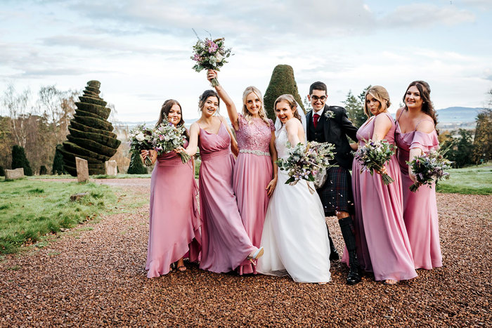 bride, groom and five pink bridesmaids pose for a photo holding out their flowers