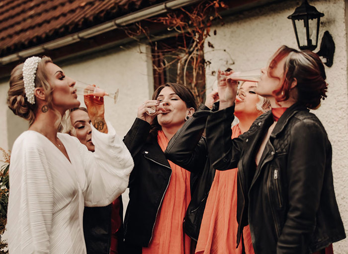 a bride and bridesmaids drinking from champagne flutes outside a dappled stone building