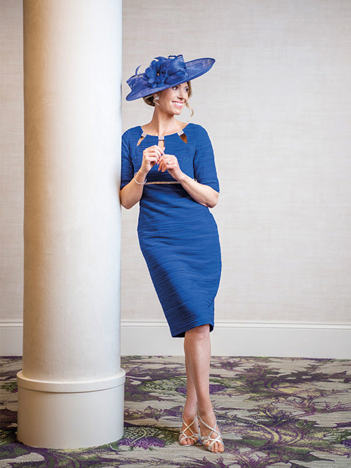 A blonde woman wearing a blue knee-length dress and a blue fascinator 