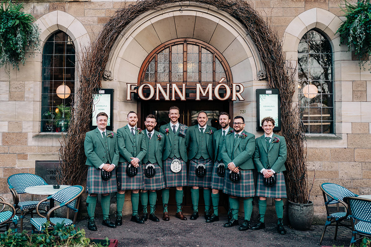 groom and groomsmen line up outside oran mor wearing green jackets and kilts