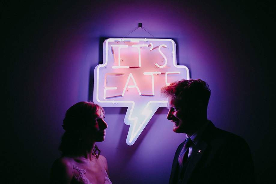 two people posing in front of a neon sign reading 'It's Fate'