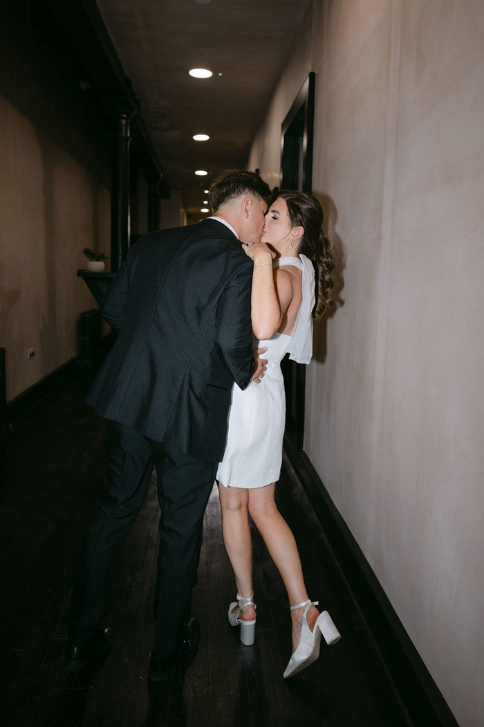 a bride wearing a short dress kissing a groom in a hallway at the Engine Works