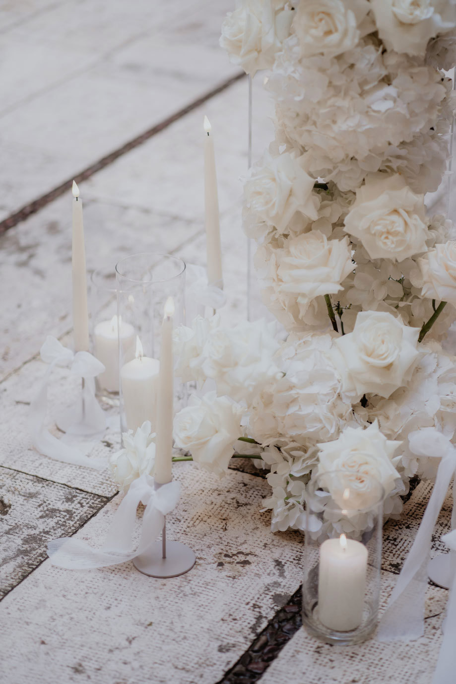 an arrangement of white candles and white flowers on a stone floor