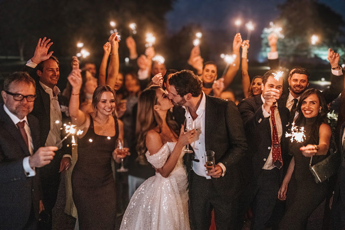 a bride and groom kissing as people around them hold sparklers.