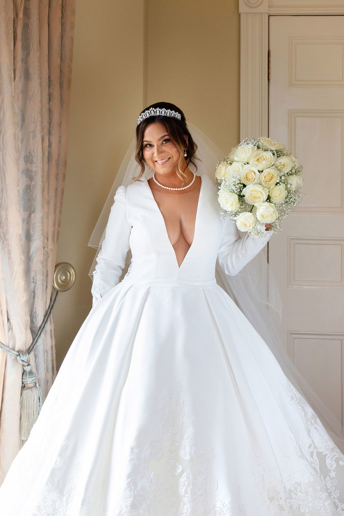 a smiling bride wearing a white dress posing with a bouquet of white roses.