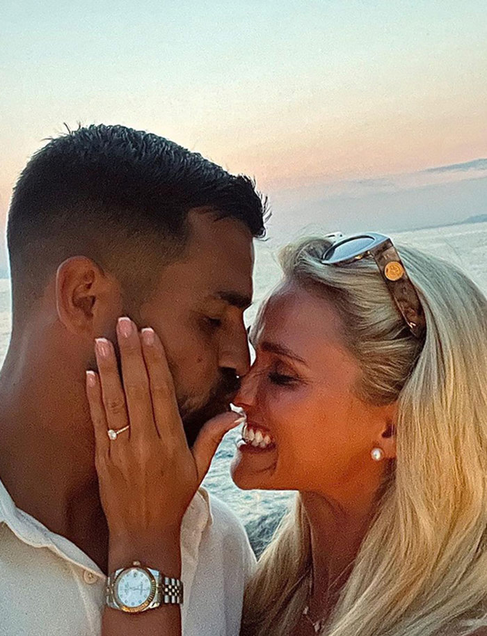 a close-up of a man kissing a woman on the nose as she shows off an engagement ring