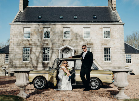 a bride and groom wearing sunglasses posing by a vintage yellow car outside Elrick House in Aberdeen