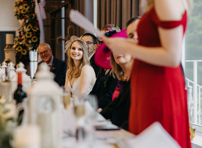 A woman in a red dress holding a piece of paper as she gives a speech to a long table of people