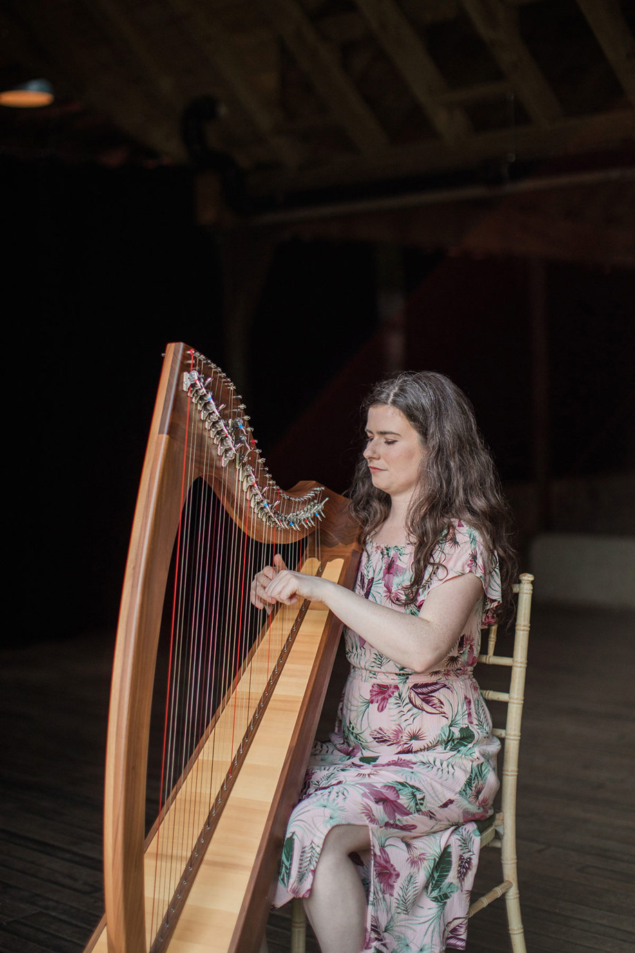 A person wearing a pink floral dress playing the harp. Emma Durkan at the Byre at Inchyra.