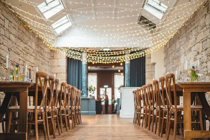 space with chairs lined up down each side facing into long trestle tables with fairylights overhead