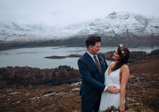 Bride and groom smile at each other in front of snow-capped mountain