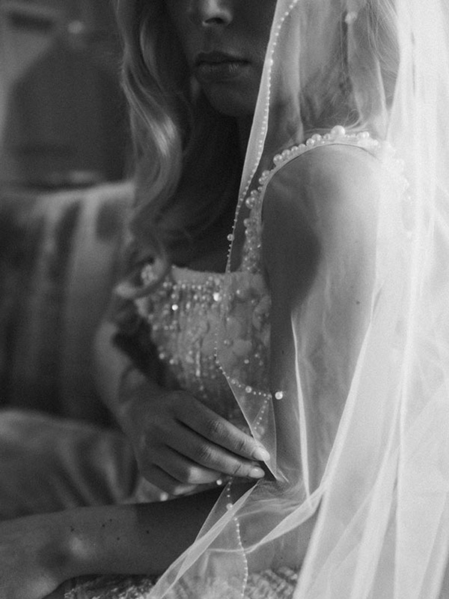 a close up black and white image of a bride in a sparkly embellished dress with a long veil draped over her shoulder