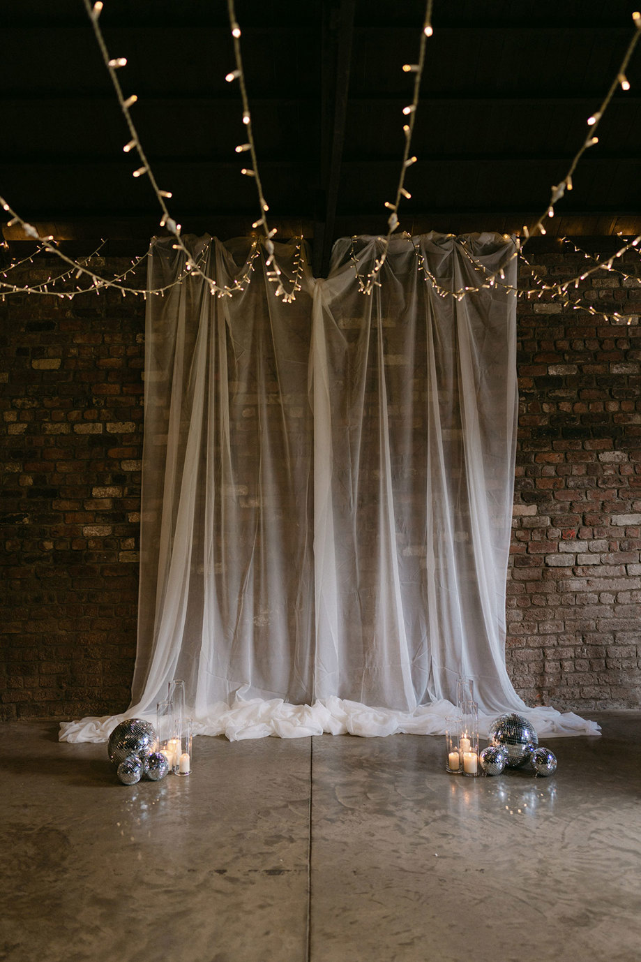 A white curtain, lights and disco balls in front of a brick wall